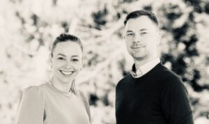 Smiling woman on the left and man on the right posing outdoors with a blurred natural background.
