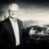 Portrait of a smiling man in a suit before a futuristic landscape with a compass, symbolizing leadership and foresight in business.