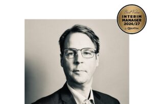 Head-and-shoulders portrait of a man in a suit and glasses, with an award badge reading 'Best Value Interim Manager 2026/27' in the corner.