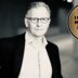Black-and-white portrait of a man in a suit and glasses next to a gold circular badge that reads 'Best Value Interim Manager 2026/27'.