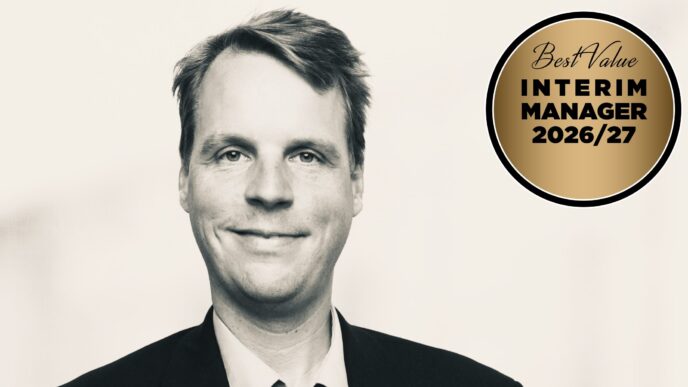 Black-and-white portrait of a smiling man in a suit with a gold circular badge reading 'Best Value Interim Manager 2026/27' on the right.