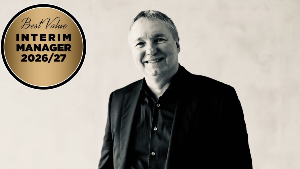 Smiling man in a black suit beside a gold circular badge that says 'Best Value Interim Manager 2026/27'.